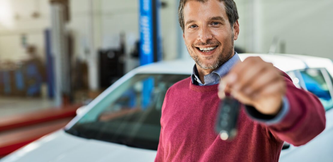 Happy man holding key of his repaired car at auto repair shop.