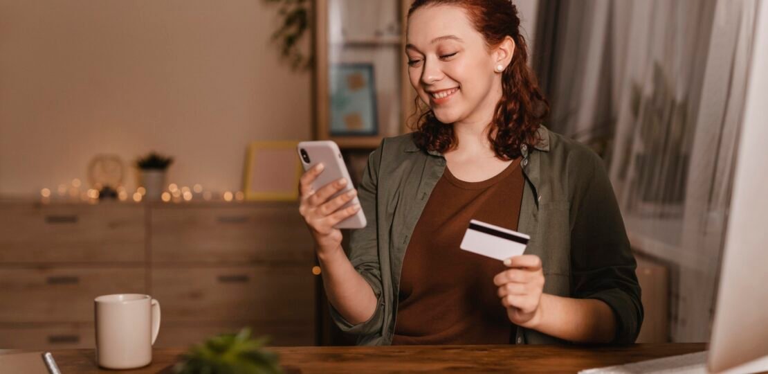 smiley-woman-using-her-smartphone-home-with-credit-card